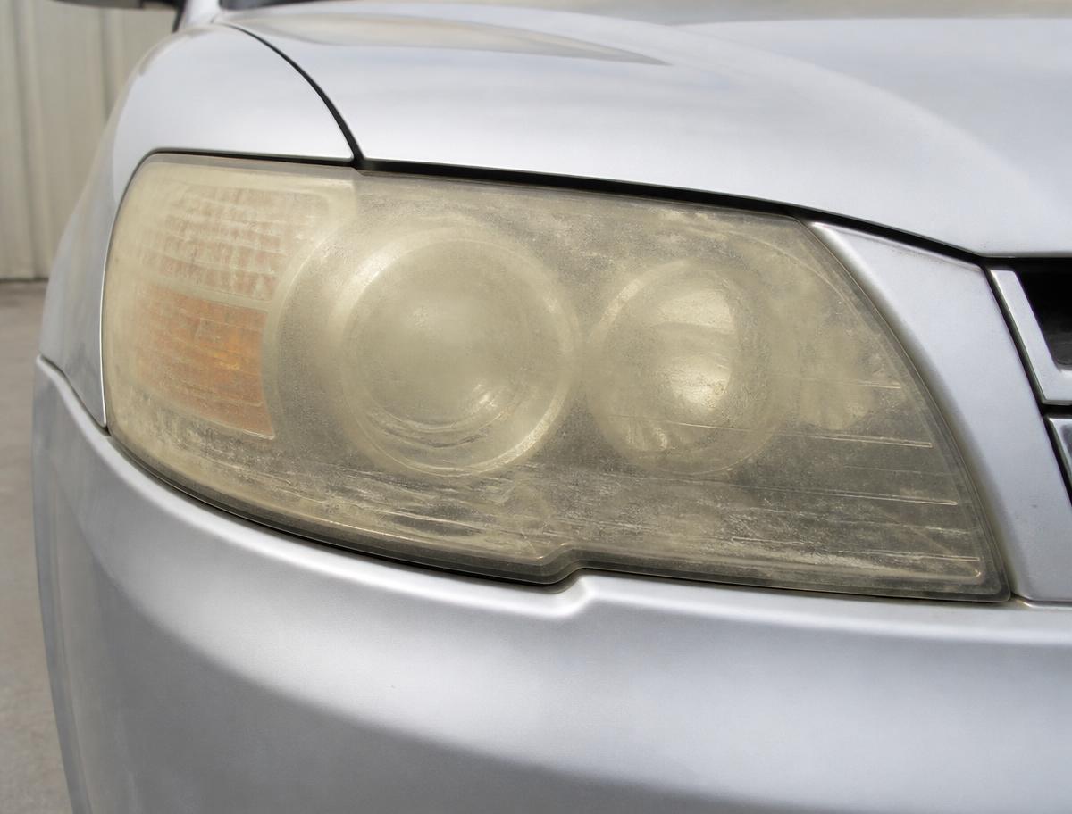 Silver SUV headlight before restoration, heavily yellowed and hazy